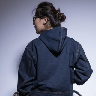 Une femme de dos avec un chignon et une combinaison en jean avec une capuche.