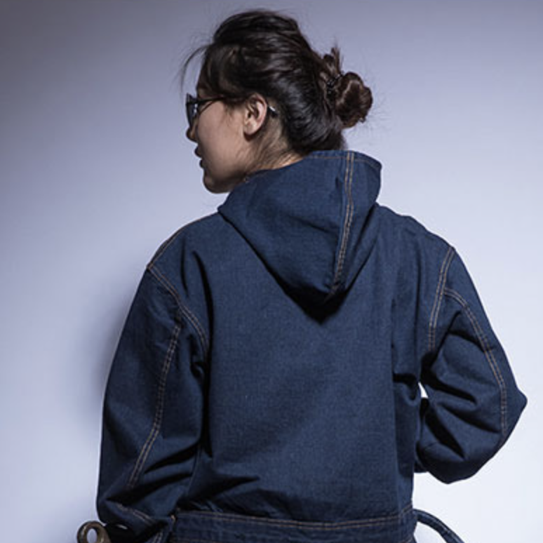 Une femme de dos avec un chignon et une combinaison en jean avec une capuche.