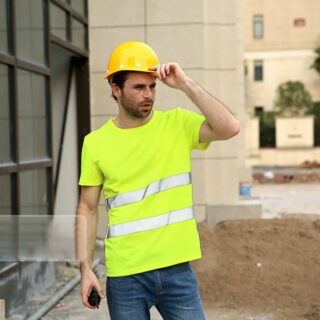 On voit un artisan sur un chantier BTP, il porte un casque jaune et un T-shirt haute visibilité.