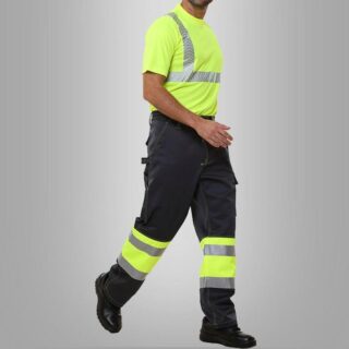On voit un homme en vêtements de haute visibilité qui marche sur fond gris. Le pantalon est jaune avec des bandes réfléchissantes.