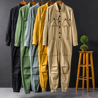 Photo de plusieurs combinaison mulit-poches, de différentes couleurs suspendues sur un fond noir avec un tabouret en bois et une plante dessus en arrière plan